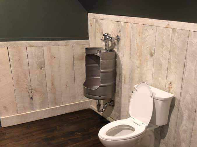 Bathroom with a wall-mounted keg urinal and a toilet against a wooden panel wall.