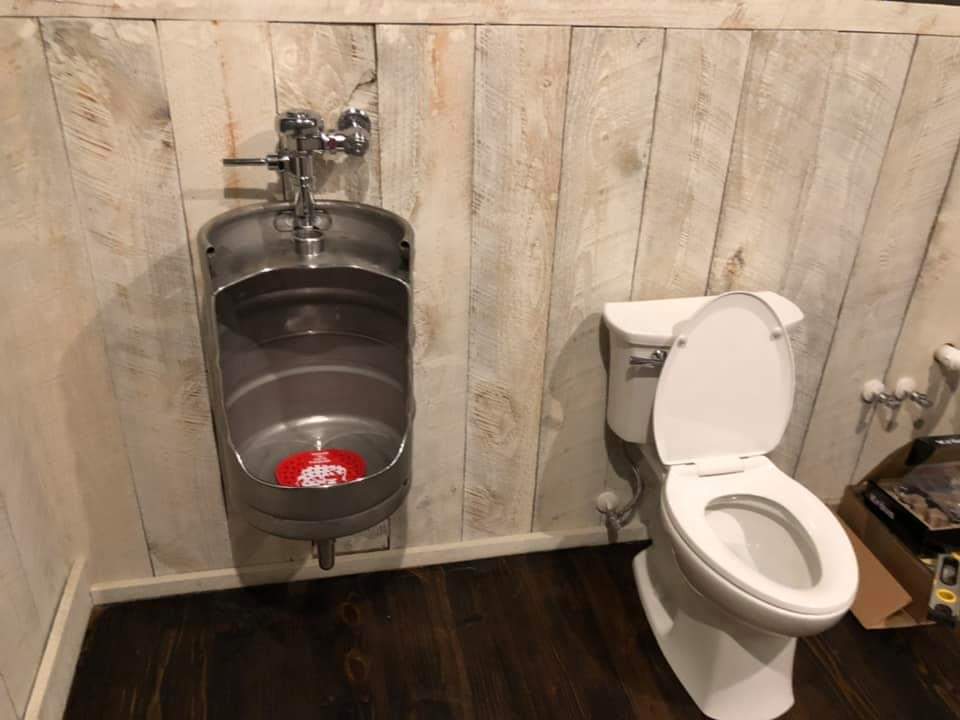Bathroom with keg urinal and toilet against a wooden panel wall.