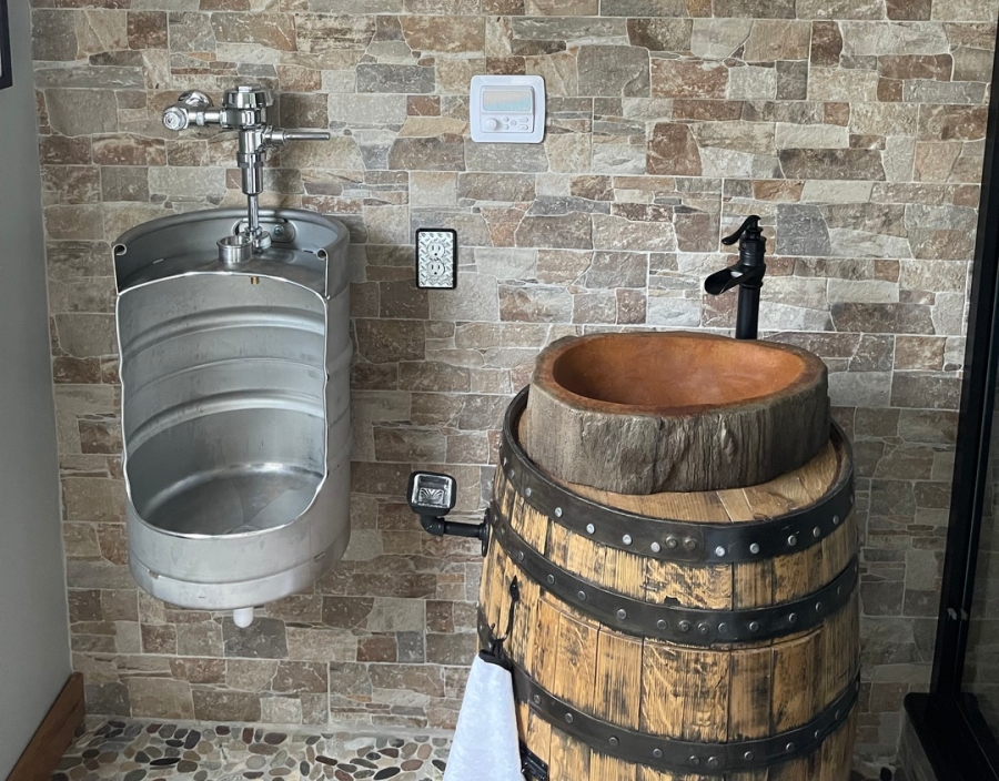 Bathroom with stone wall, keg urinal, and wooden sink on a barrel